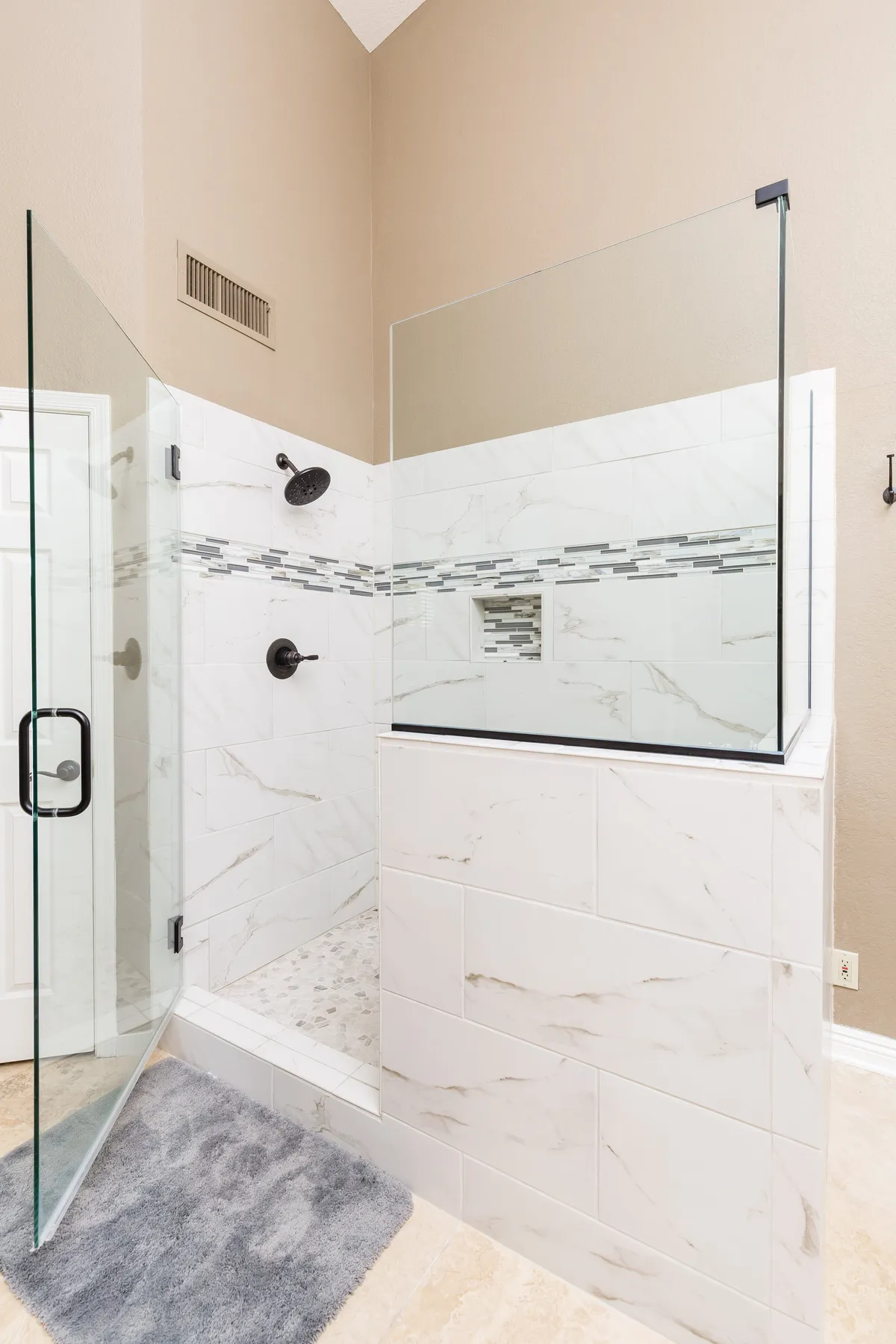 A pristine bathroom with a glass shower enclosure, marble tile finishes, and a decorative mosaic strip. The space is bright and tranquil, highlighting modern fixtures and a spa-like ambiance.