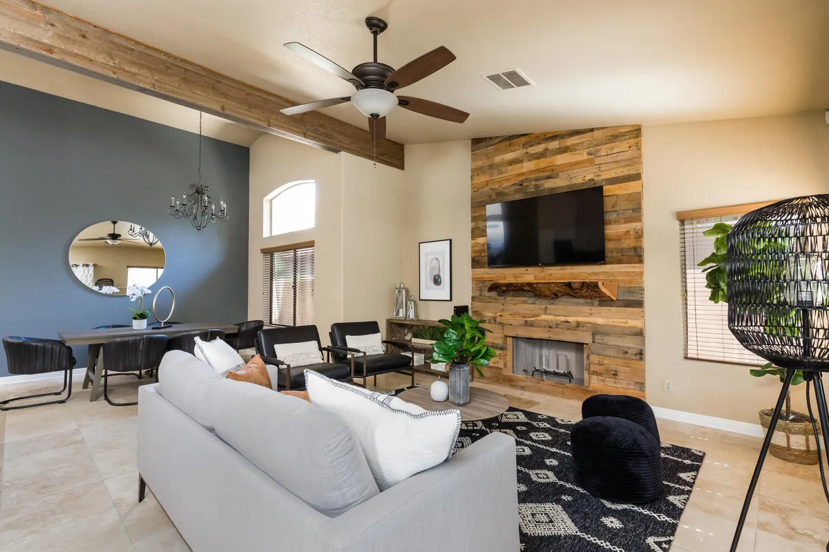 A stylish and comfortable open-concept living and dining area featuring a cozy sofa, wooden accent wall, modern chandelier, and a chic dining table accented by lush green plants. The space exudes warmth, is bathed in natural light, and is perfect for both relaxing and lively conversation.