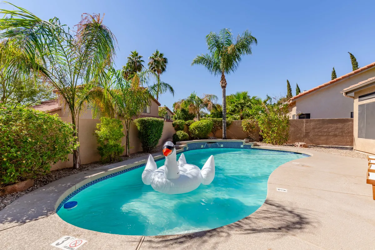 A vibrant pool scene featuring a giant swan float, palm trees, and both adults and children enjoying themselves by the water. Adults lounge poolside while children play, hinting at the space’s versatility for both relaxation and lively gatherings. The mood is playful and welcoming, reflecting family fun and memorable get-togethers.