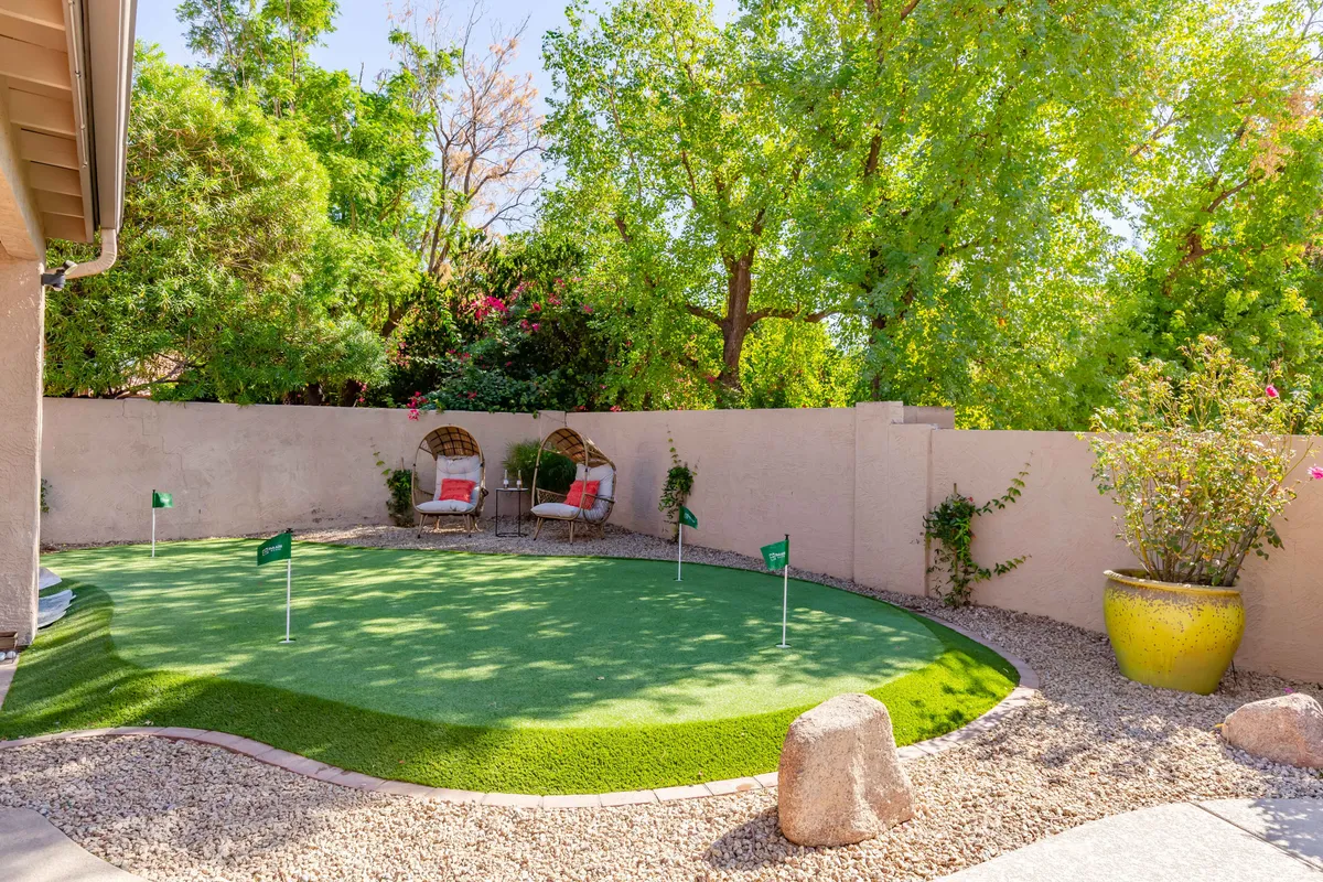 This exterior image showcases a private putting green surrounded by lush landscaping, a charming seating area, and a decorative planter. The scene is intimate and inviting, with hints that this could be a backyard or resort-style amenity, perfect for friendly competitions or relaxing after a day on the main courses.