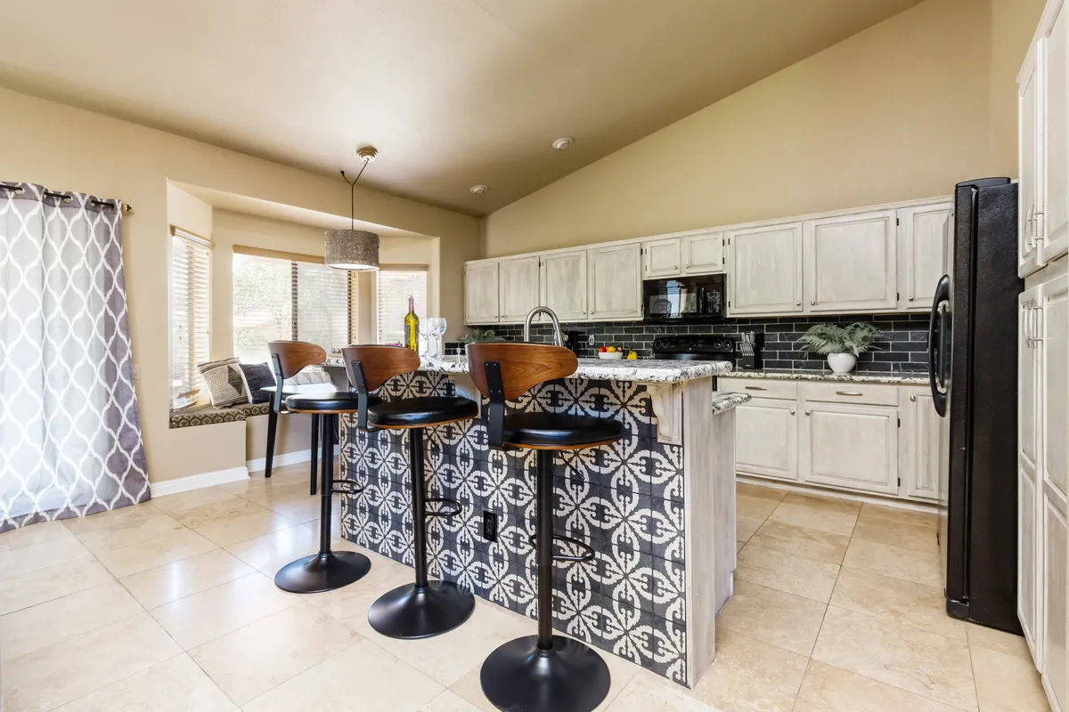 A bright, welcoming kitchen featuring a stylish island with bar stools, modern kitchen appliances, and a window seat adorned with cushions. The space is designed for cooking, entertaining, and casual dining, with thoughtful touches like ample seating and natural light.