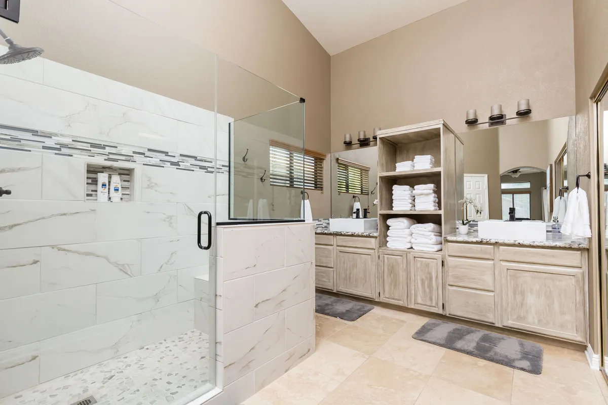 A sophisticated bathroom featuring a glass shower enclosure, double sink vanity, and a towel storage unit. The space is modern and exudes a calm, spa-like atmosphere, ideal for personal care routines and unwinding.